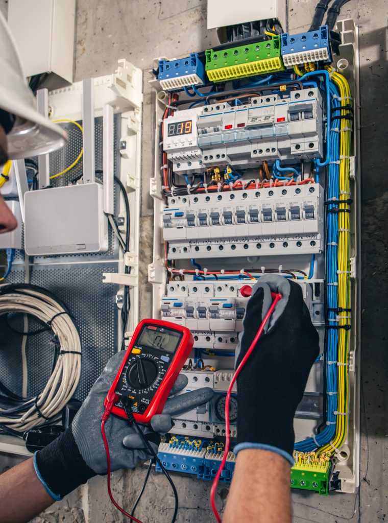 Man, an electrical technician working in a switchboard with fuses. Installation and connection of electrical equipment. Professional uses a tablet.